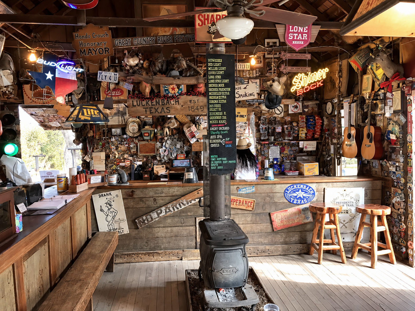 The wonderfully cluttered interior of the historic Luckenbach general store and bar, filled with vintage signs, license plates, guitars, memorabilia, and an old cast-iron stove.