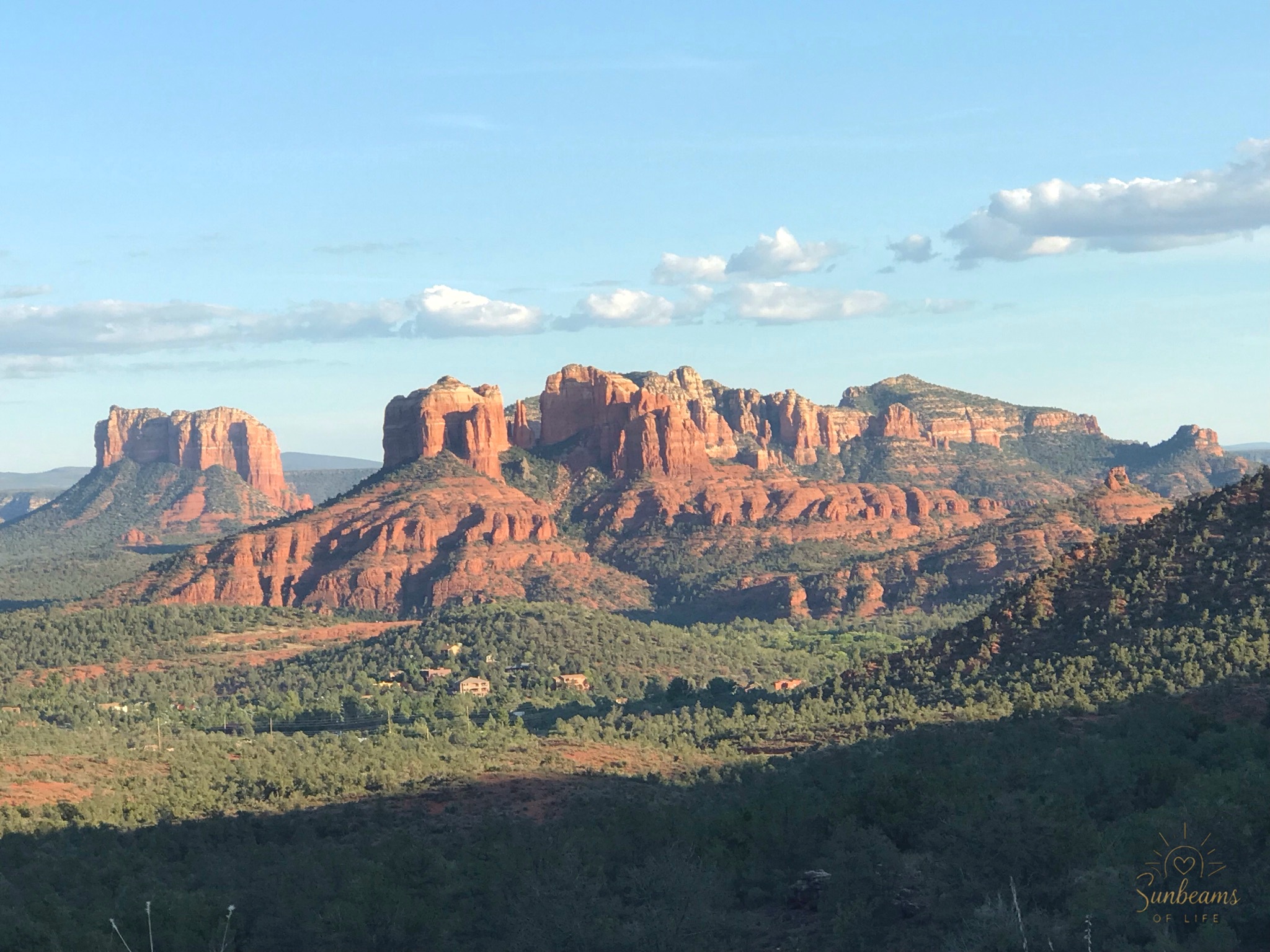 Red rock mountains rising above a green valley beneath a wide blue sky.
